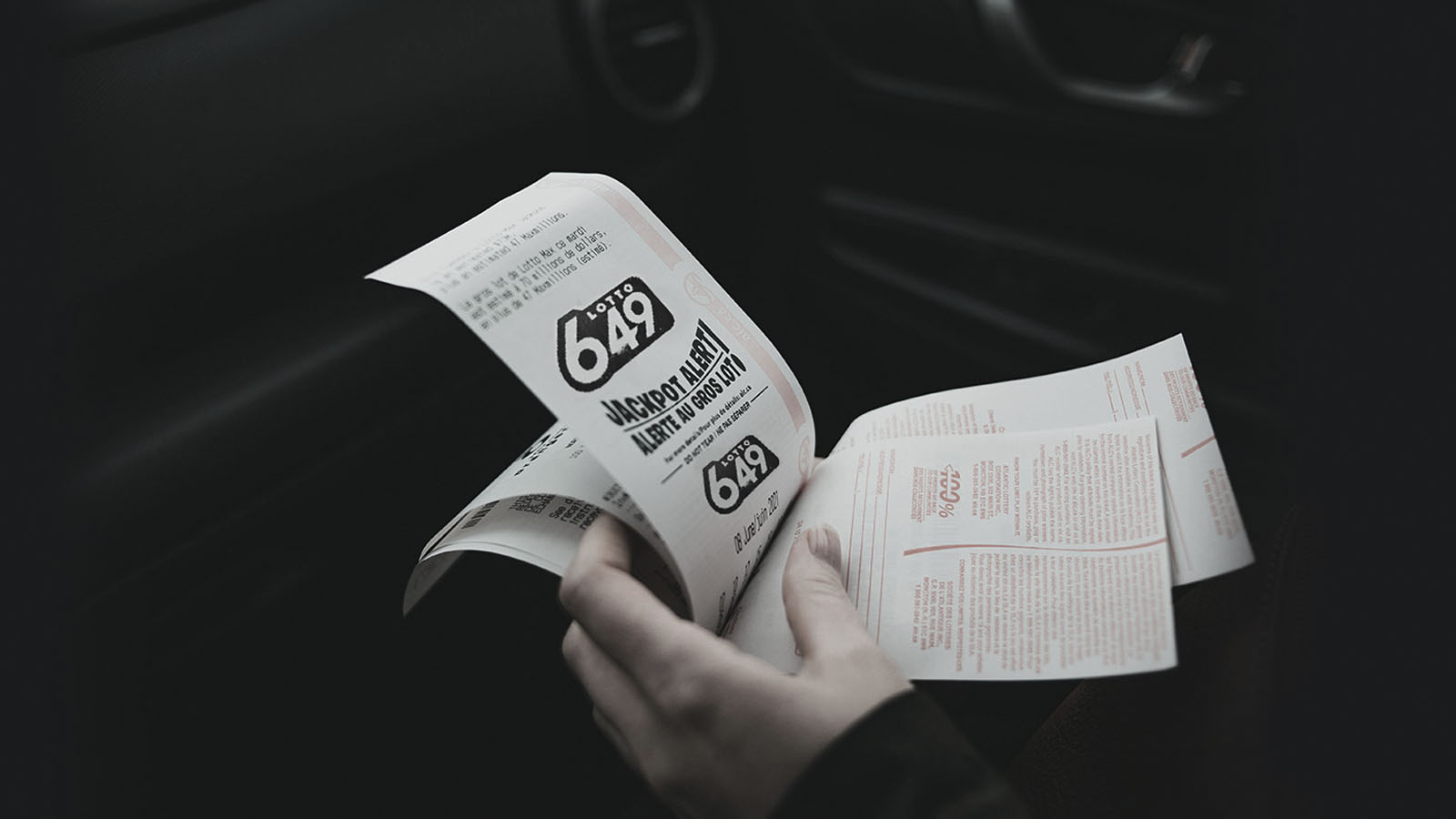 Person holding lottery tickets in their car