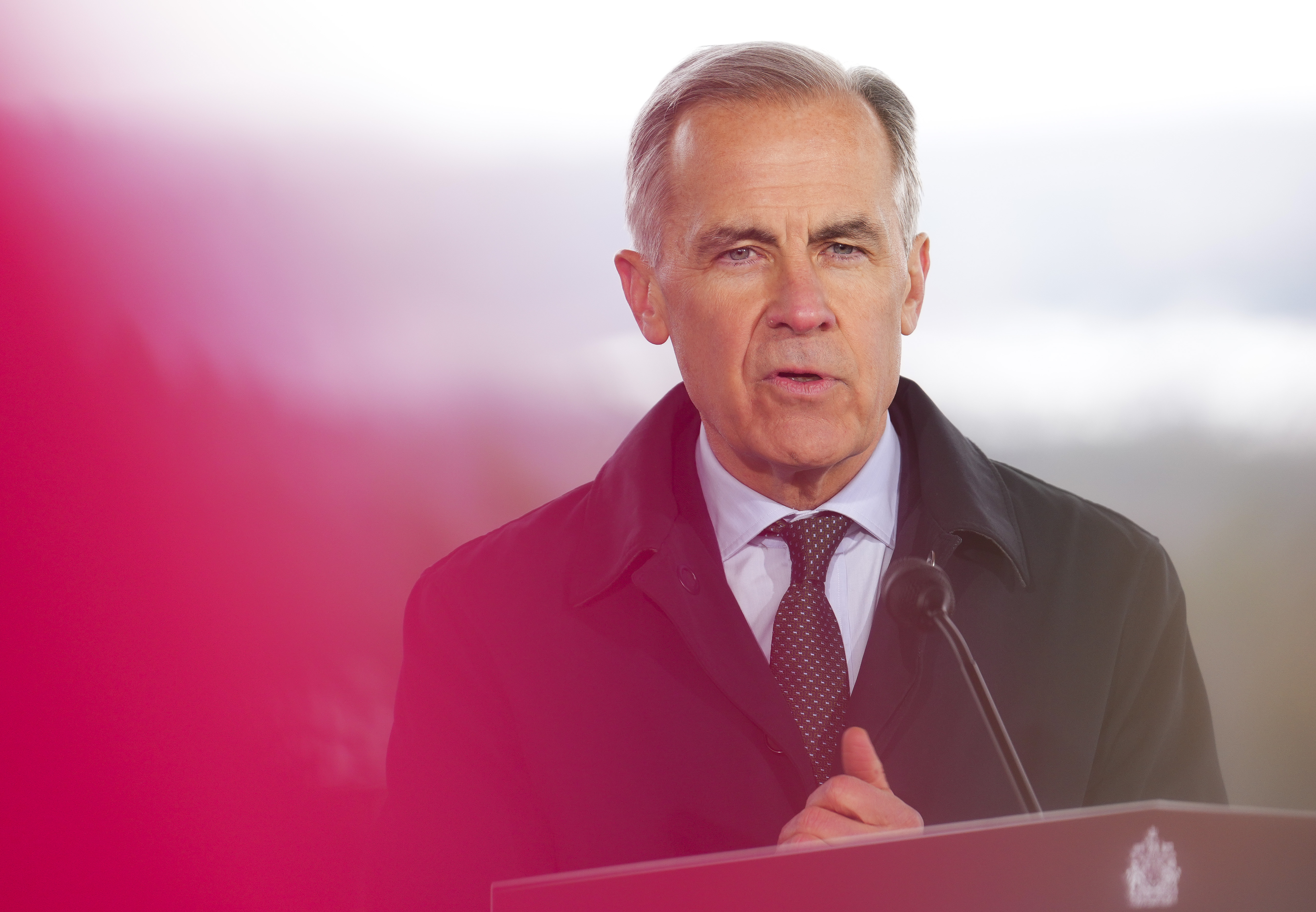 Prime Minister Mark Carney listening to a reporters question while standing at a podium during a press conference.