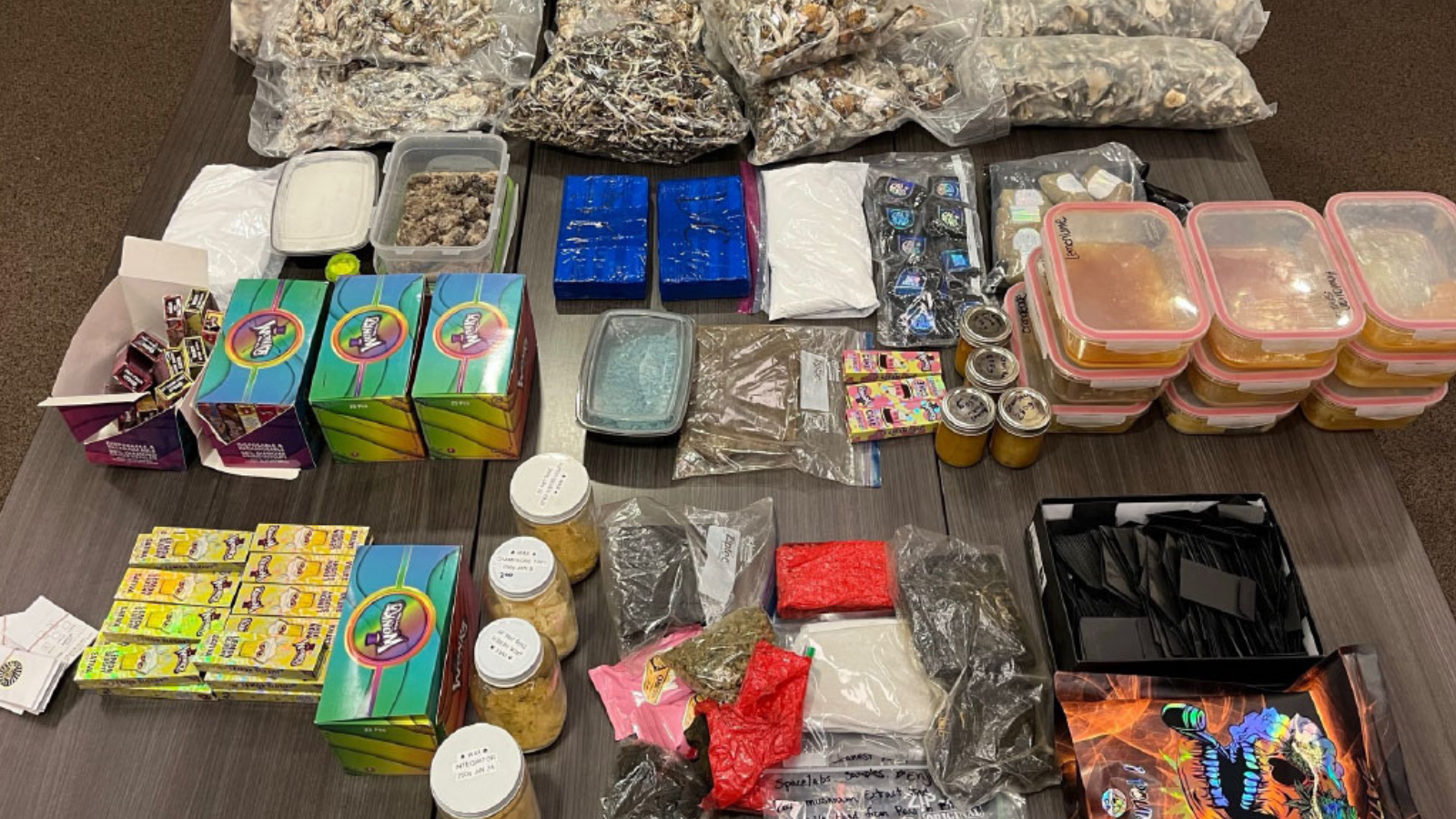 A close-up image of drugs seized by police, including vape pens, dried cannabis, alongside plastic bags and containers of unknown substances.