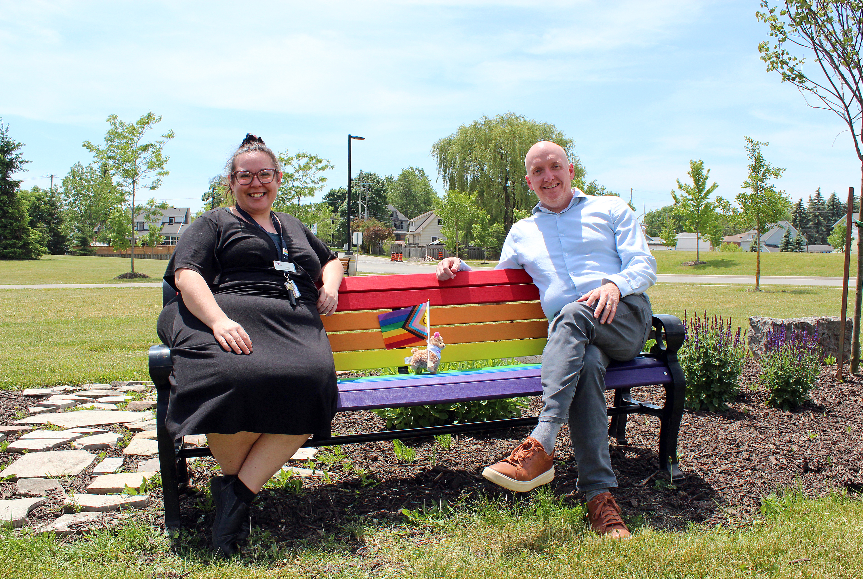 A bench painted rainbow in honour of Pride, with two people sitting on it.